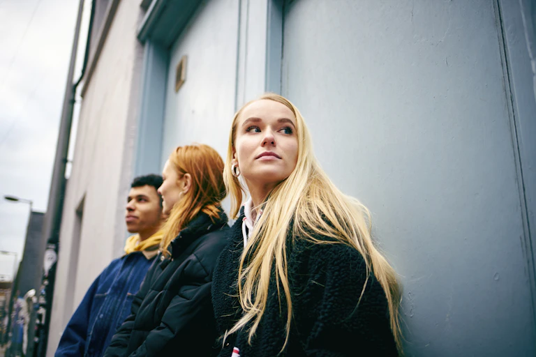 Three young people lean against a door in an alleyway.