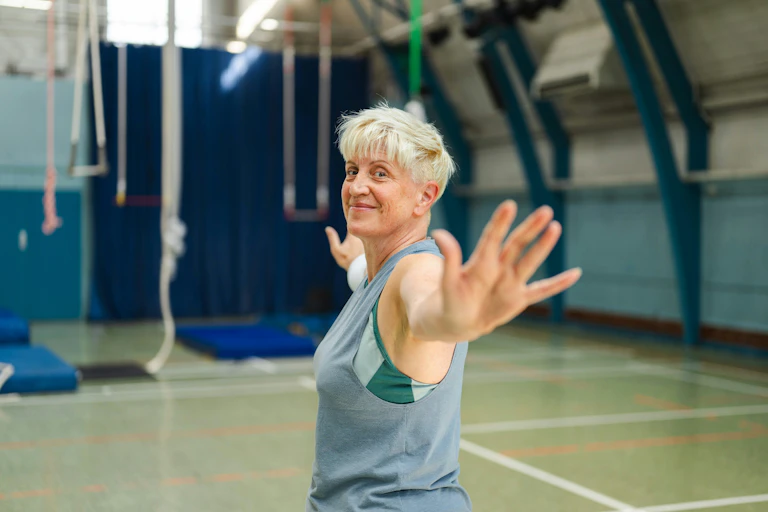 Smiling older woman stretches in a gym.
