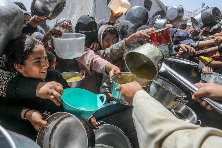 Gente que se agolpa con ollas, cazuelas y envases para recibir comida.