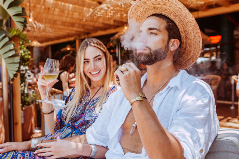 Man and woman srink wine and smoke at a beach bar