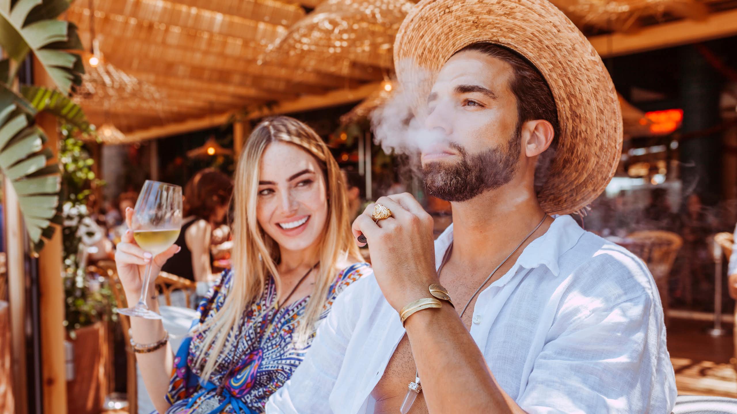Man and woman srink wine and smoke at a beach bar