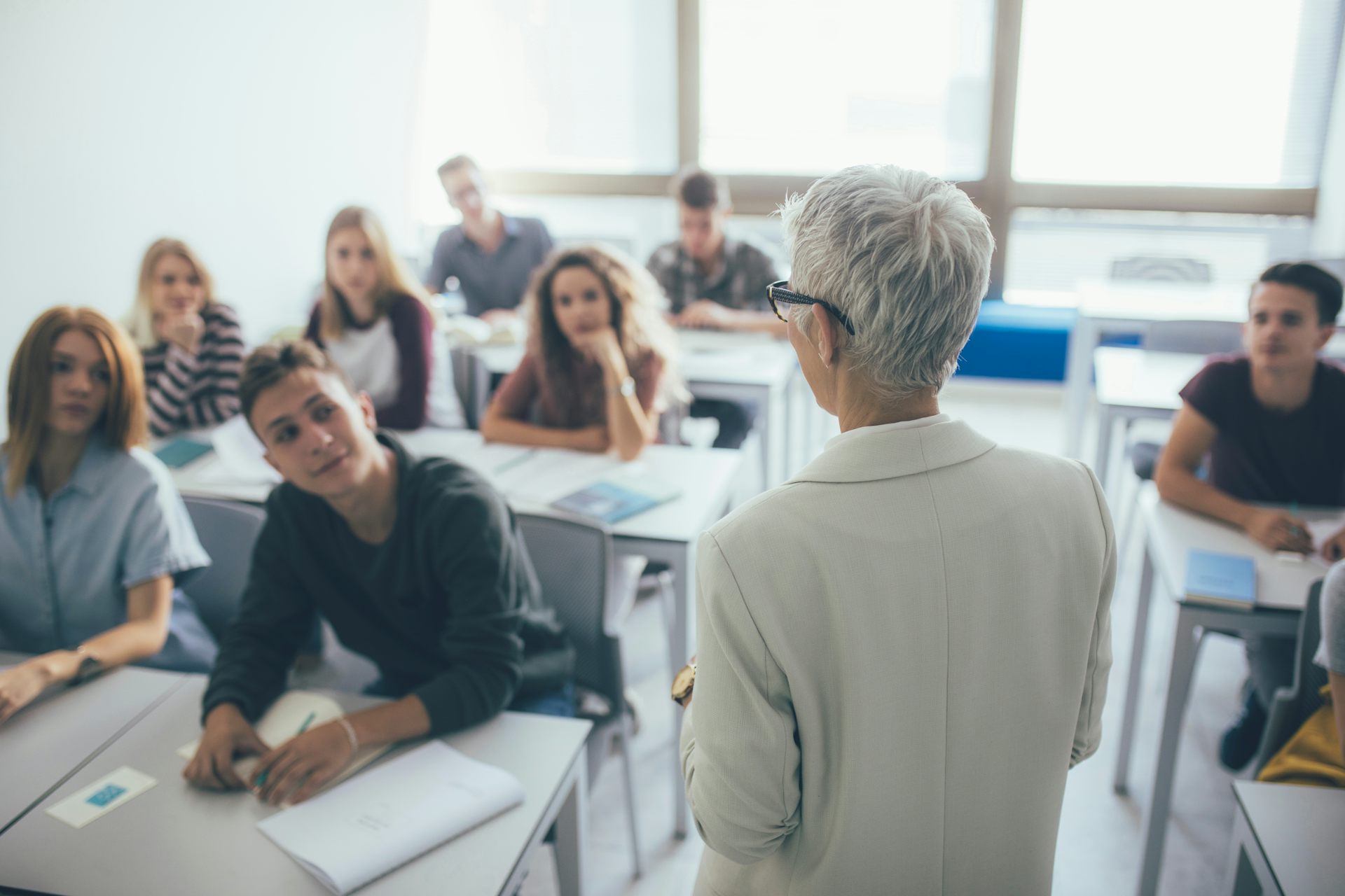 una mujer de espaldas habla a los alumnos de una clase.