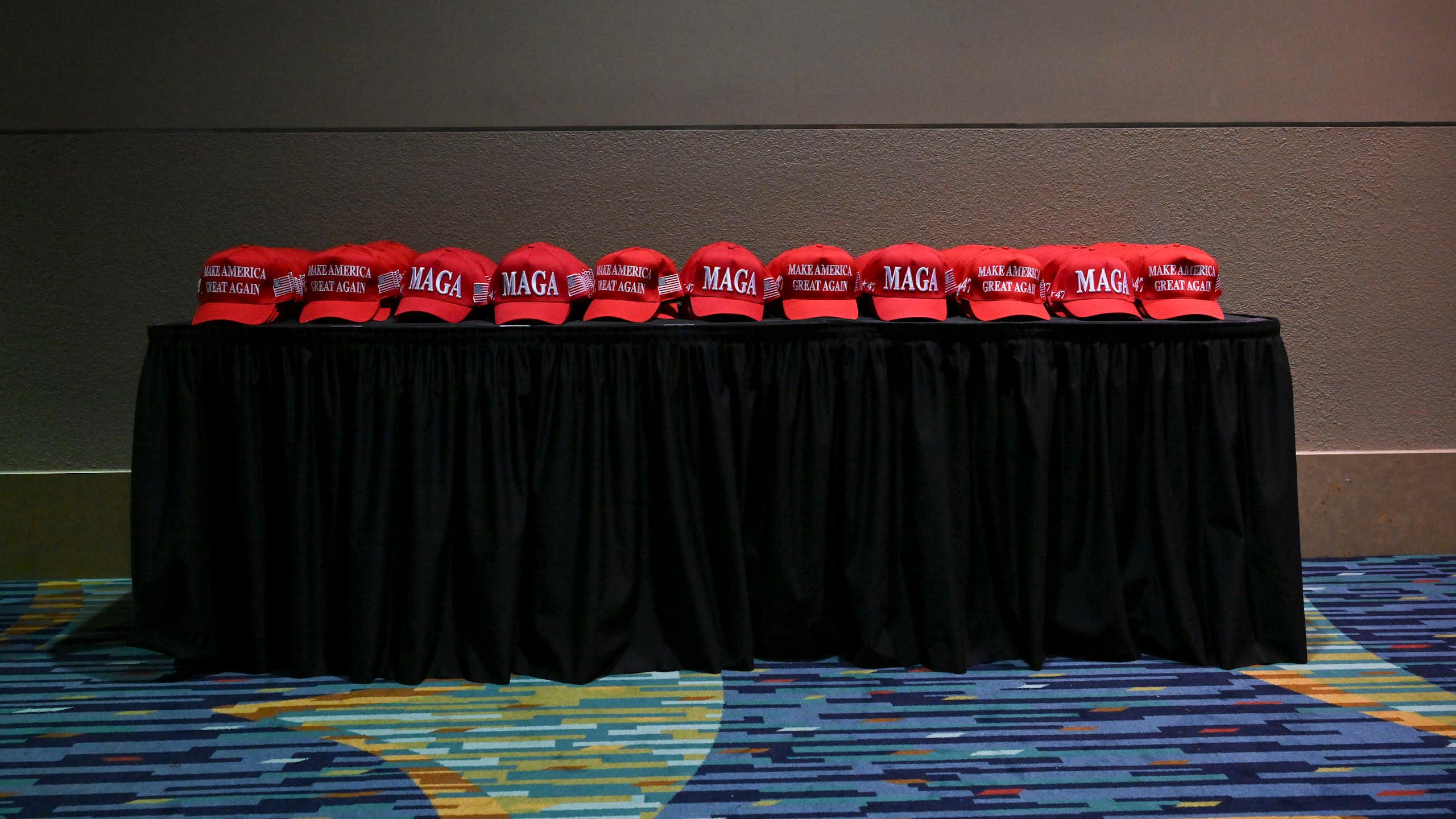 MAGA red hats are lined up on a cloth-covered table.