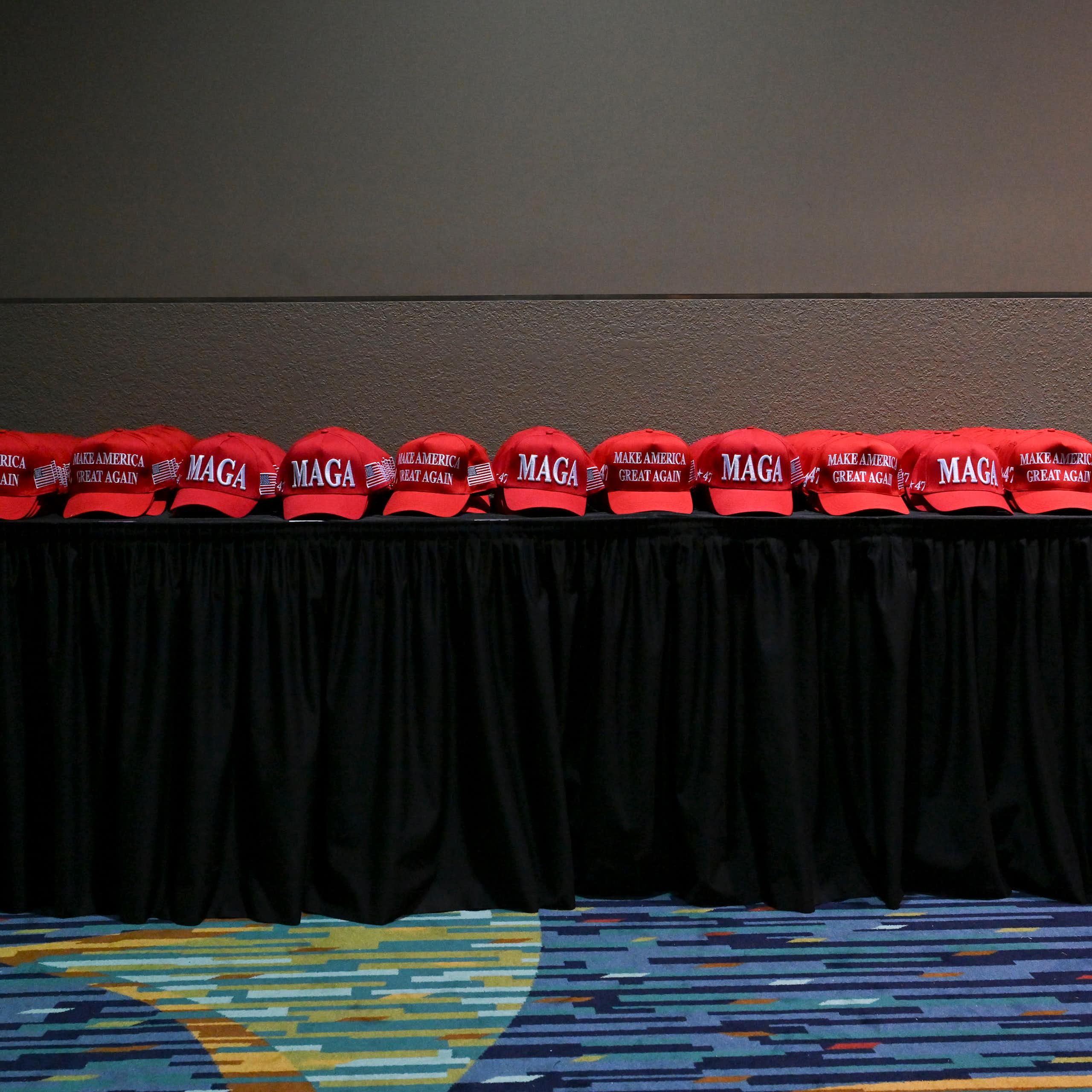 MAGA red hats are lined up on a cloth-covered table.