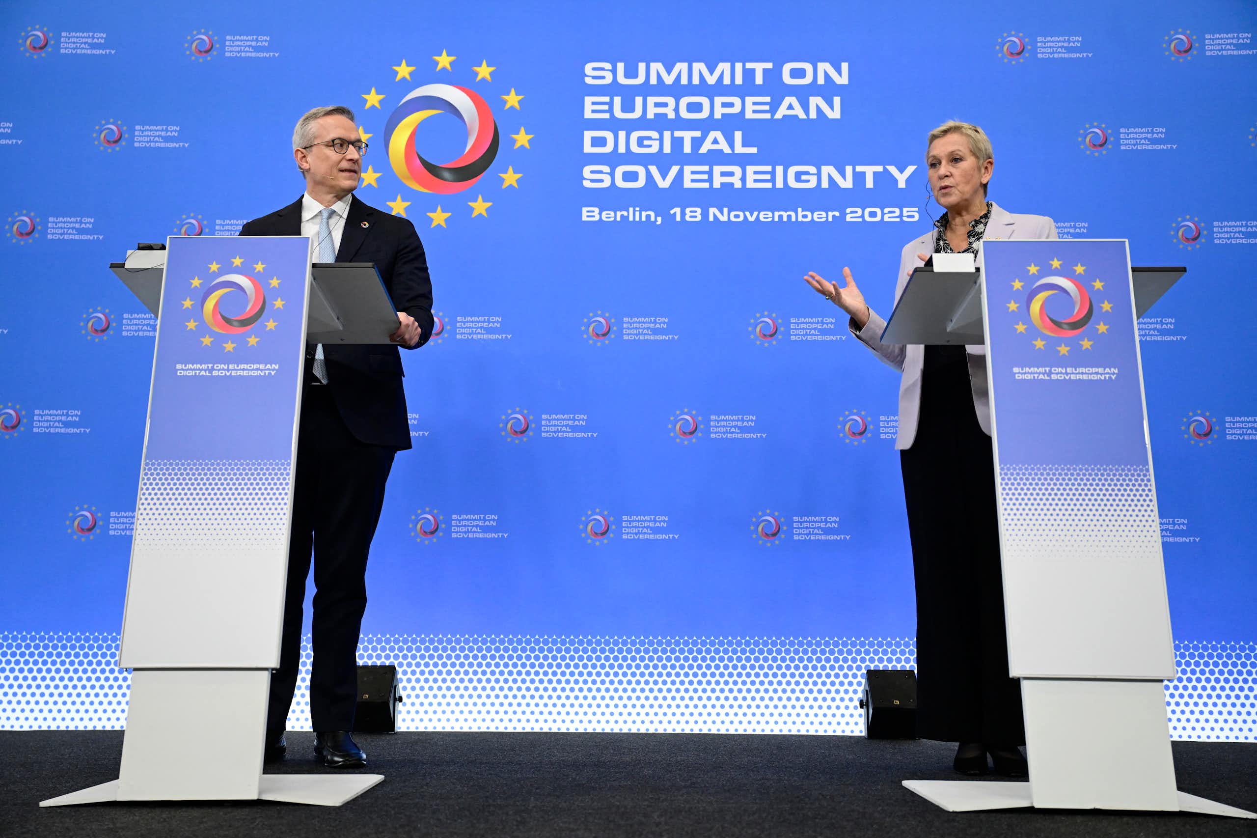 A man and a woman stand behind lecterns on a stage. The woman is speaking.