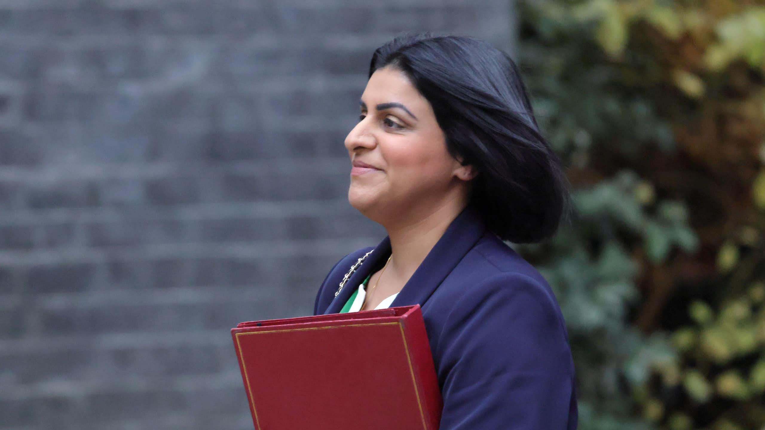 Photo of Shabana Mahmood in profile, walking with a red minister's folder