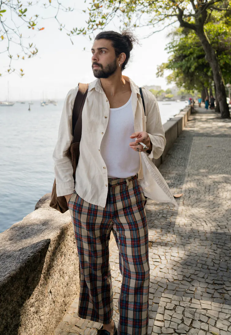 Un jeune homme avec un chignon se tient près d’un canal, un café à la main