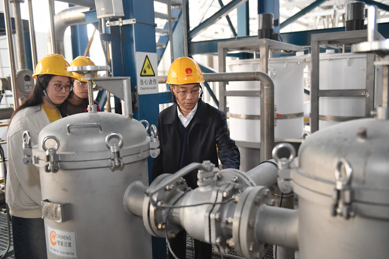 People in hard hats look at a metal apparatus.