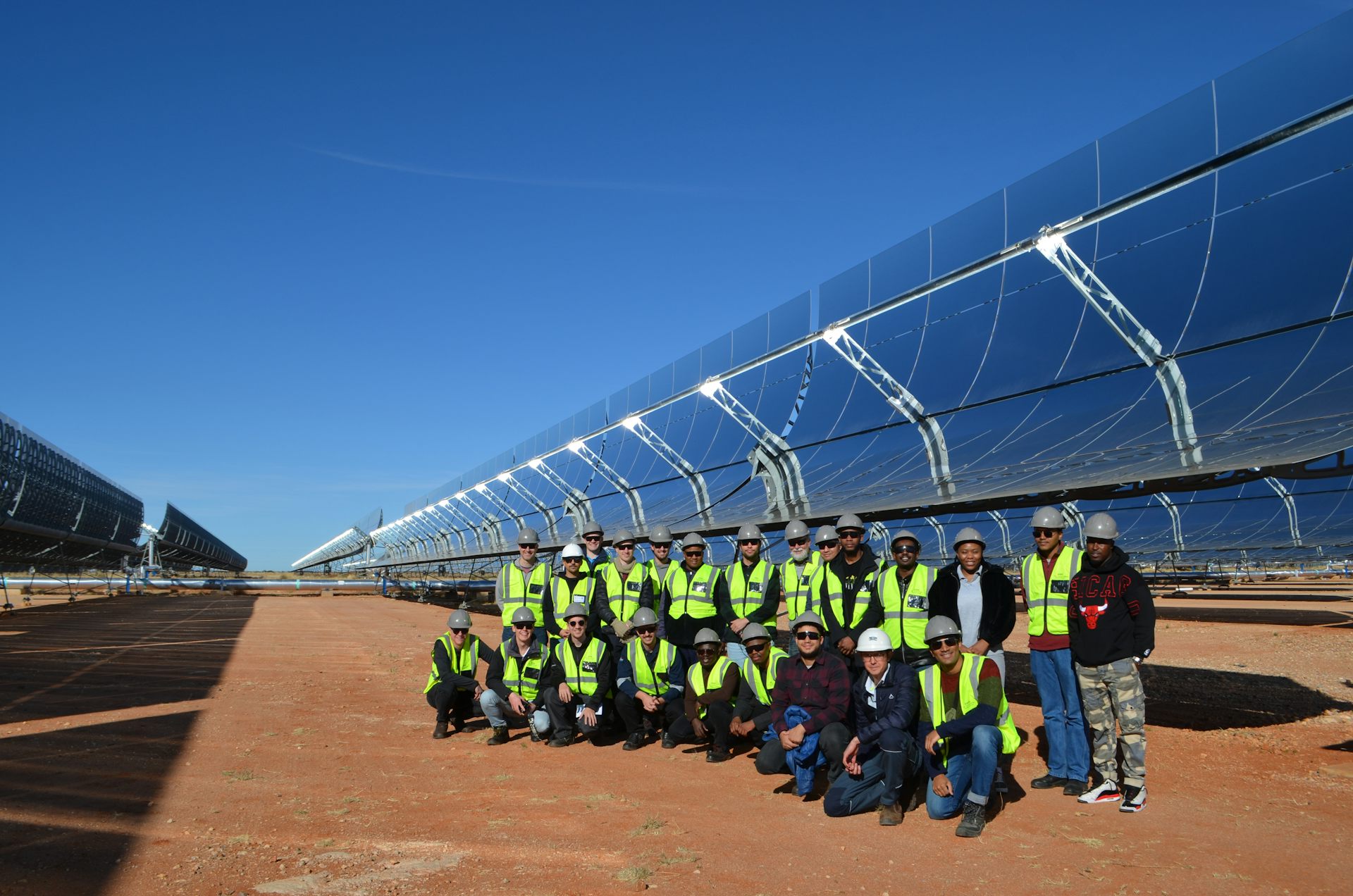 Many people lined up in front of giant solar panels mounted on the ground