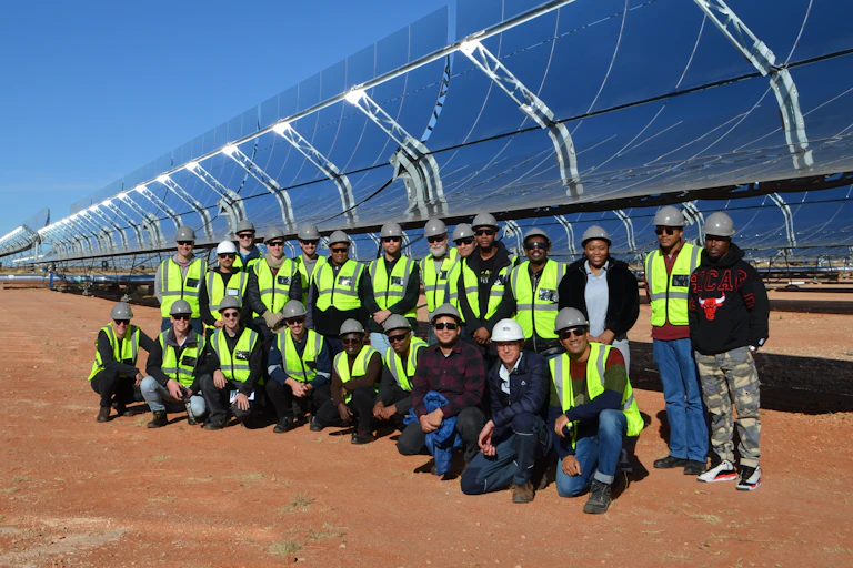 Many people lined up in front of giant solar panels mounted on the ground
