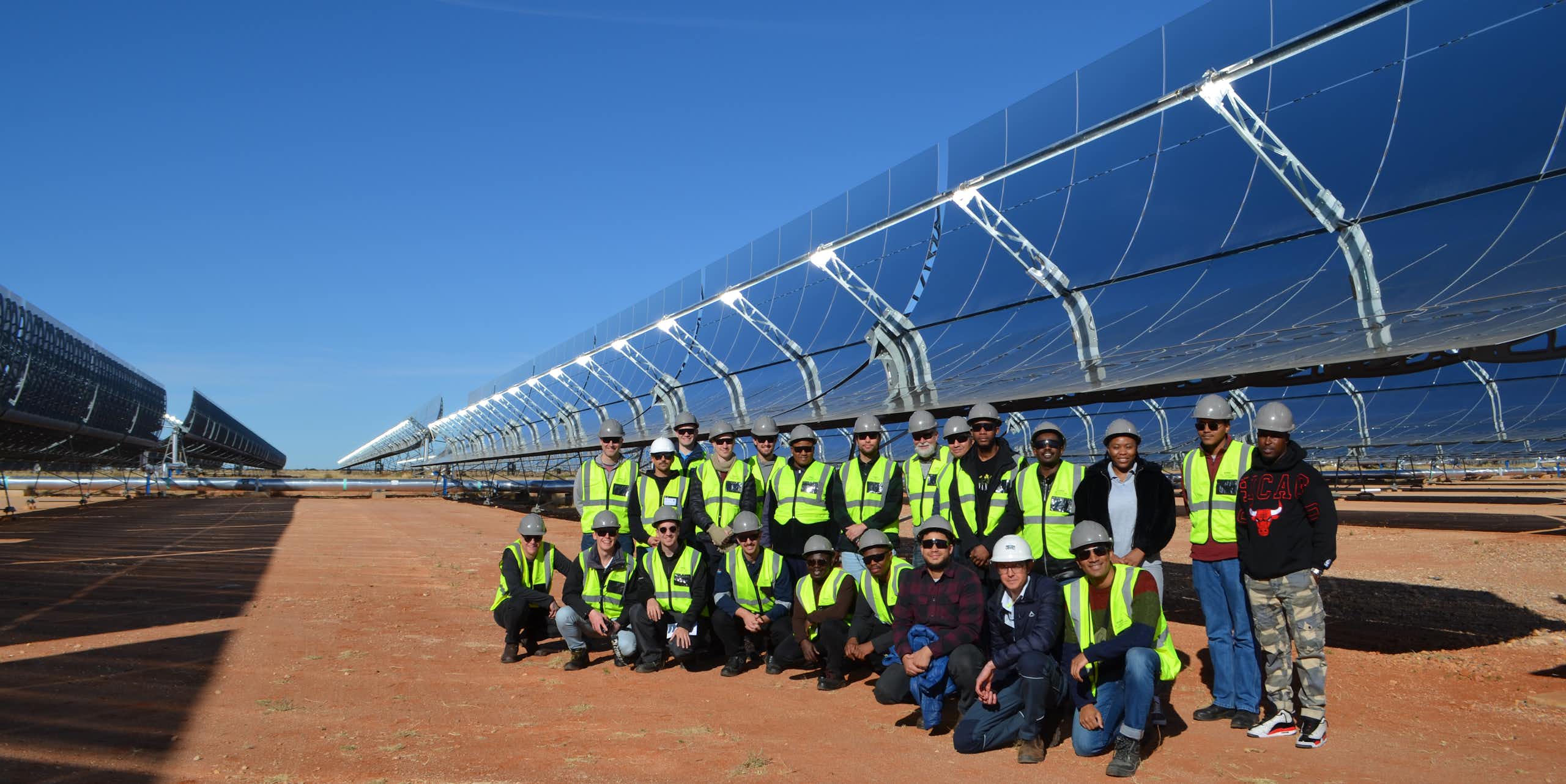 Many people lined up in front of giant solar panels mounted on the ground