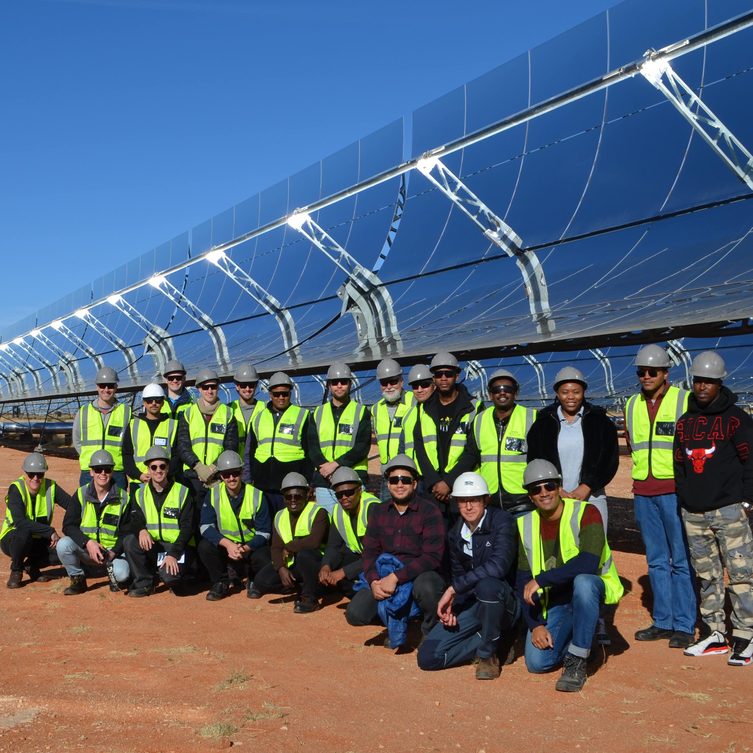 Many people lined up in front of giant solar panels mounted on the ground