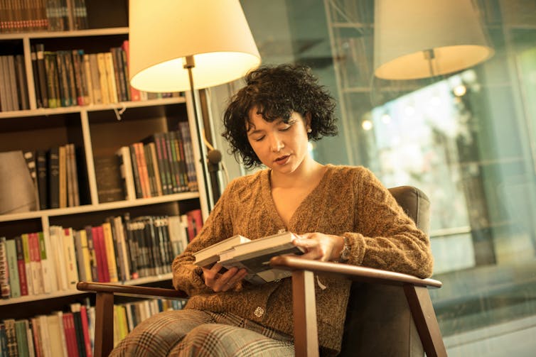 Mujer joven leyendo un libro en una silla en una librería.