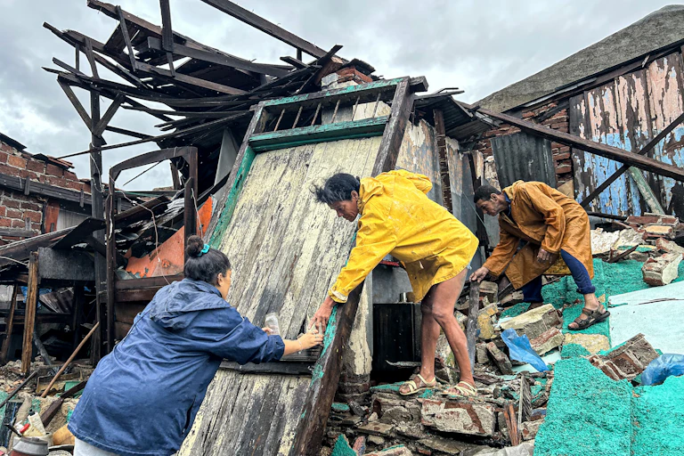 A woman reaches out to help another stop down from the debris of a storm damaged home after Hurricane Melissa.