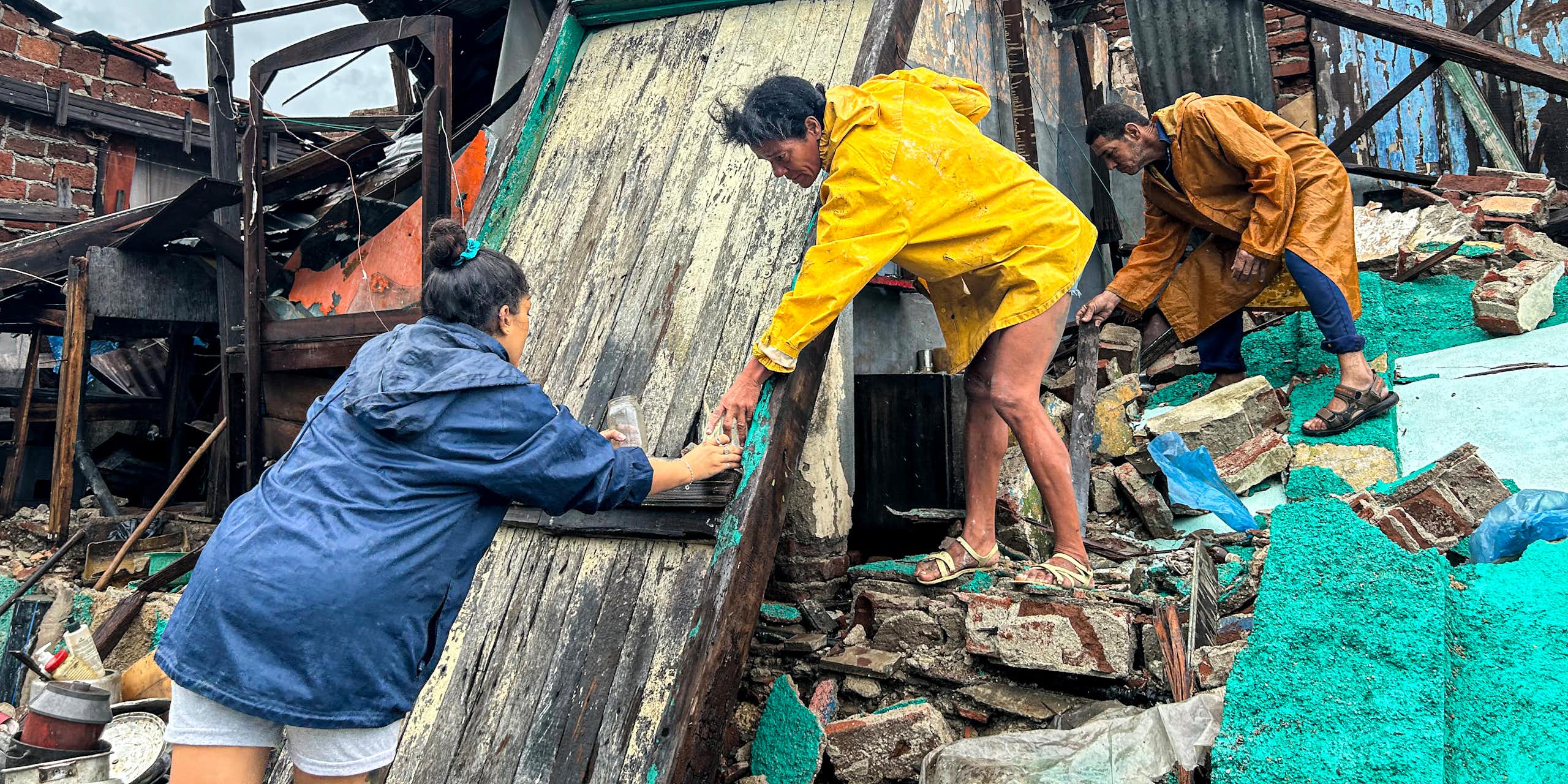 A woman reaches out to help another stop down from the debris of a storm damaged home after Hurricane Melissa.