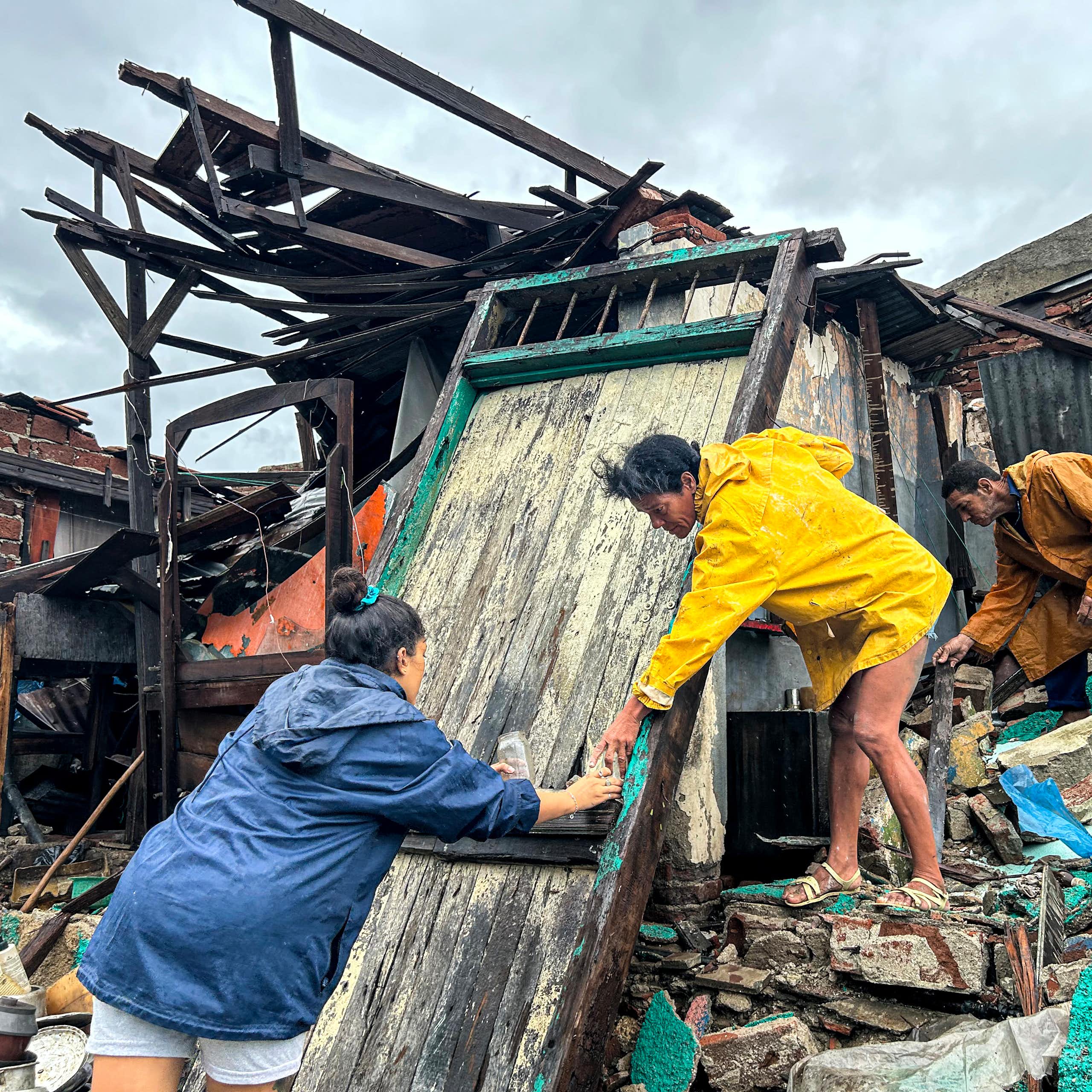 A woman reaches out to help another stop down from the debris of a storm damaged home after Hurricane Melissa.