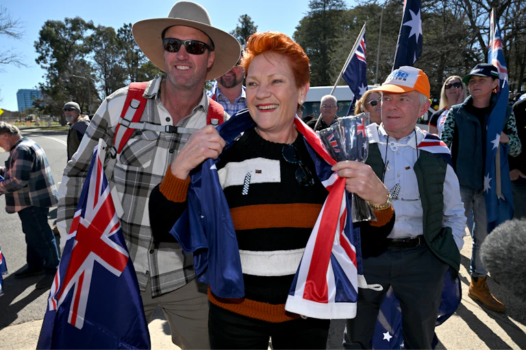 Pauline Hanson, wrapped in an Australian flag, smiles at a protest