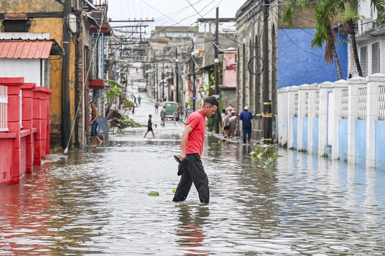 A man walks through a flooded street with water reaching into homes in Cuba.
