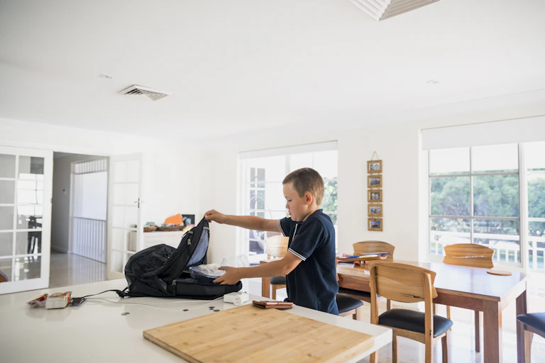 A boy packs a bag on a kitchen bench.