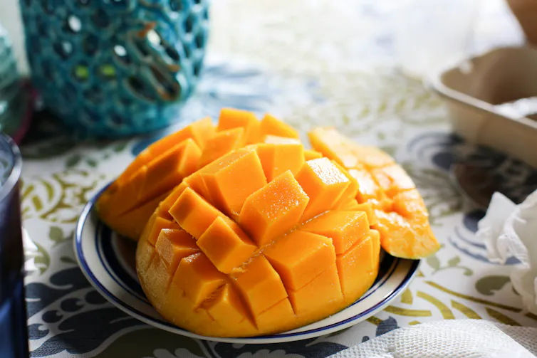 A mango has been cut and sits on a plate on a table.
