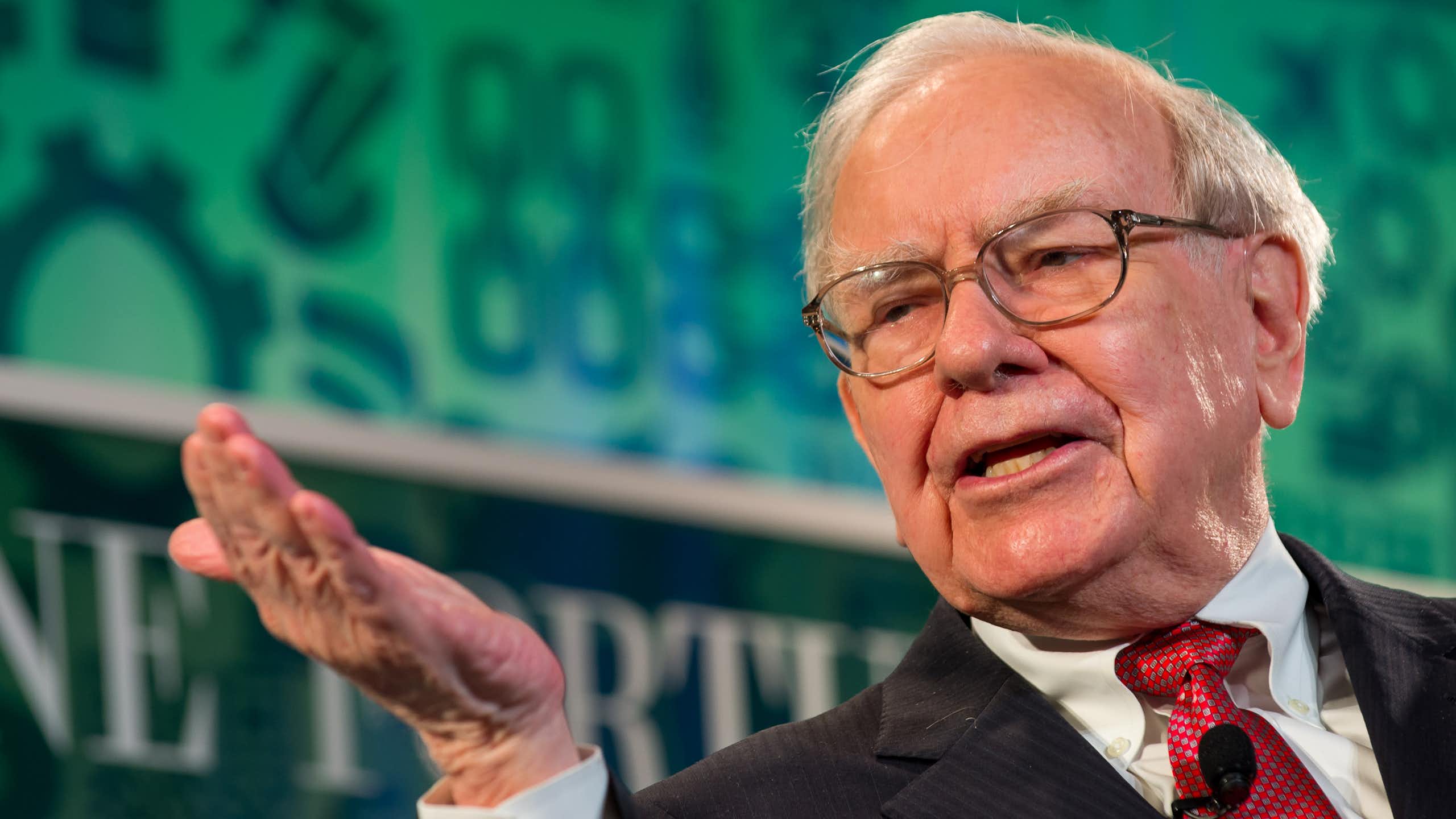 Warren Buffett wearing in a suit and tie, talking on stage.