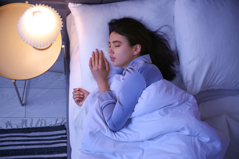 Woman asleep with lamp on bedside table left on.