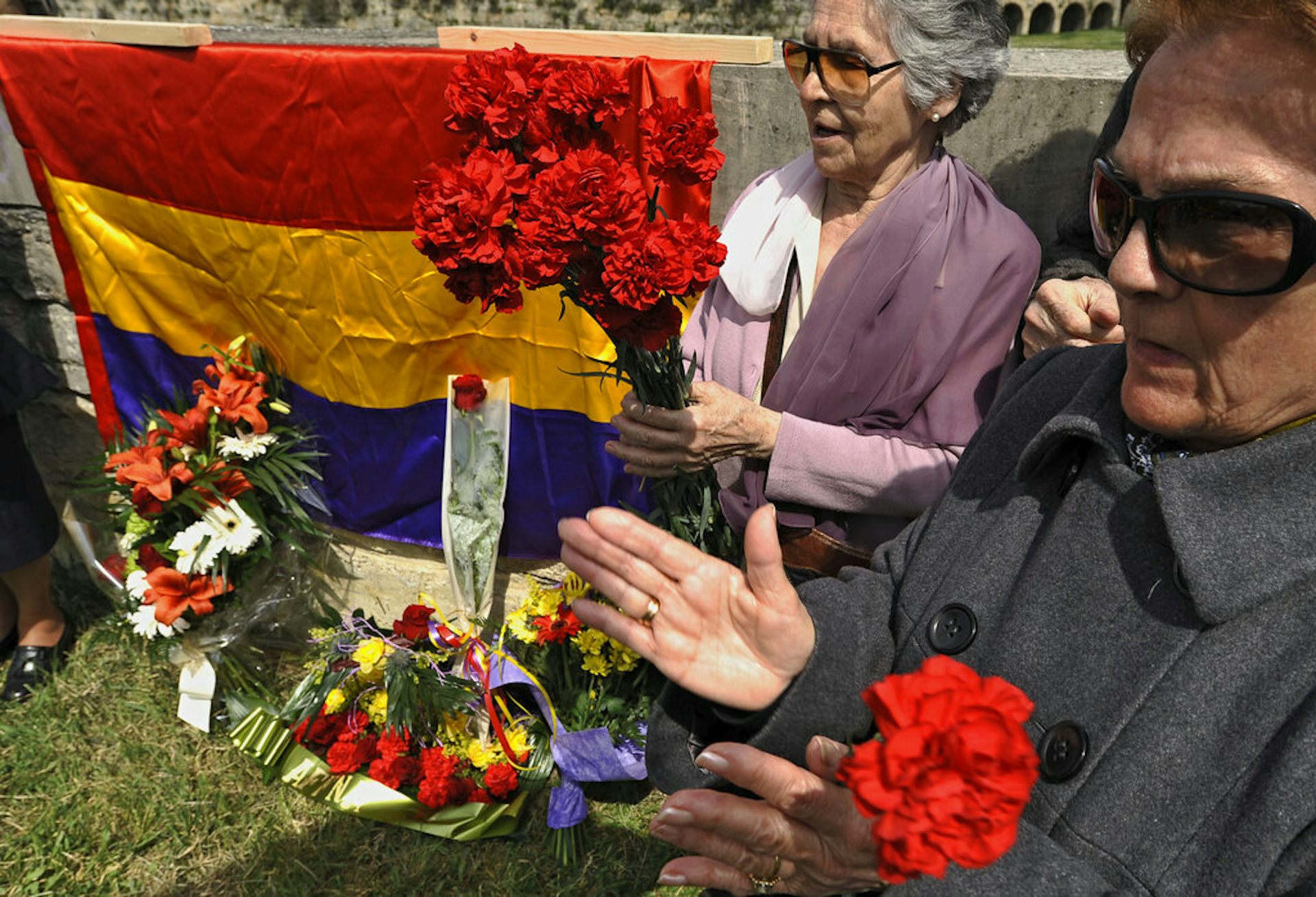 Women present flowers at a memorial.