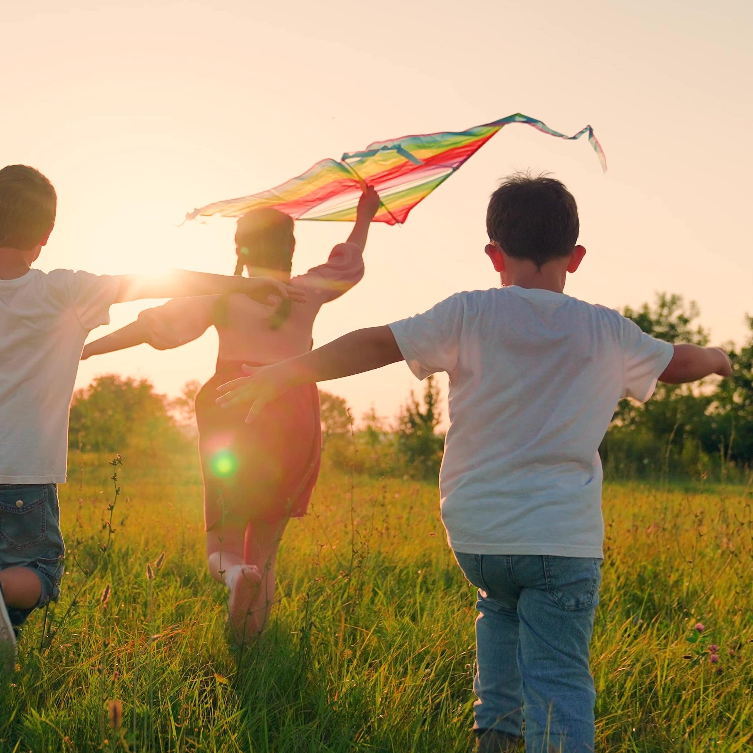 Niñosy niñas corriendo con una cometa.