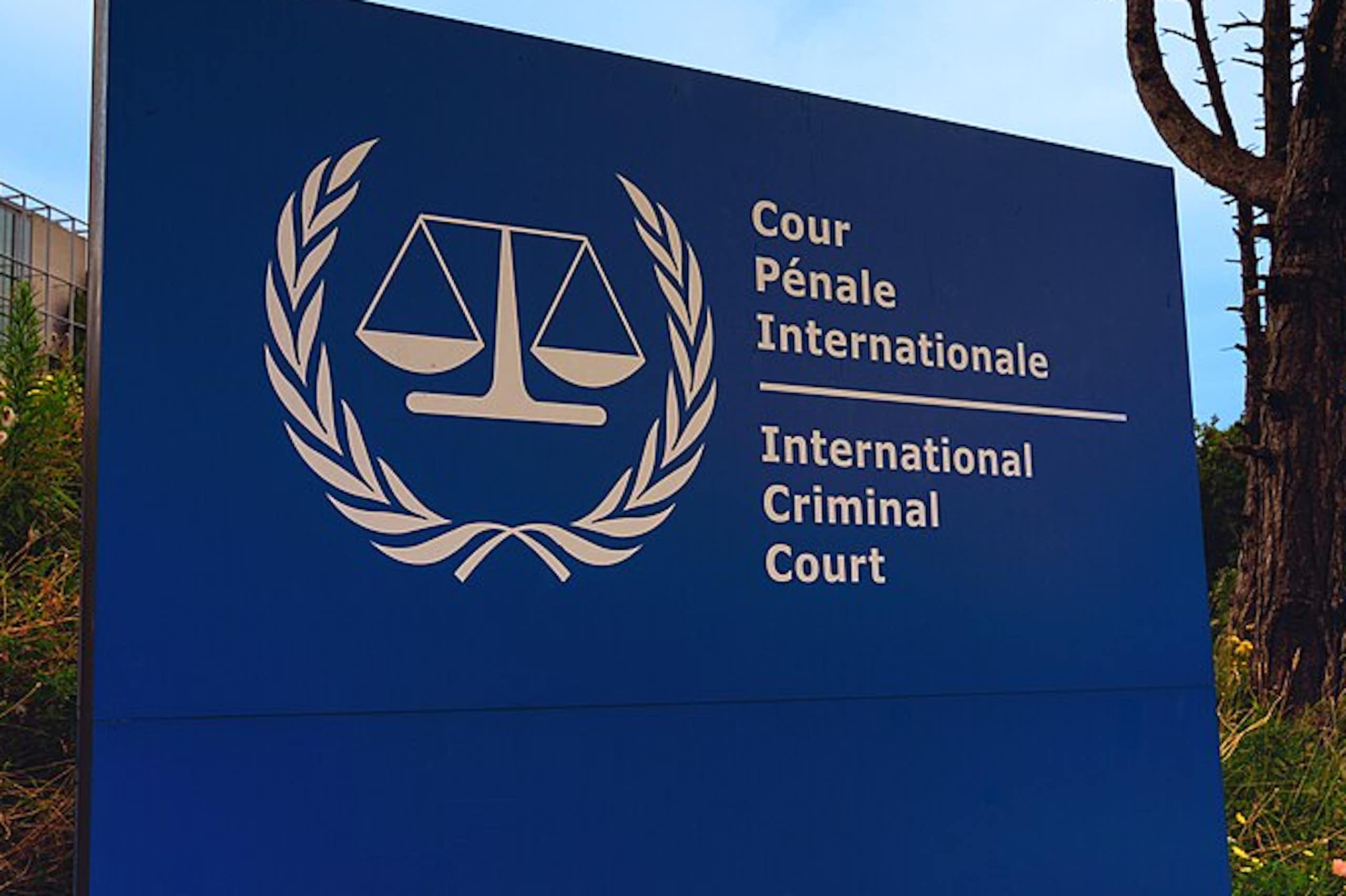 A blue and white sign reads International Criminal Court in English and French in front of a building.