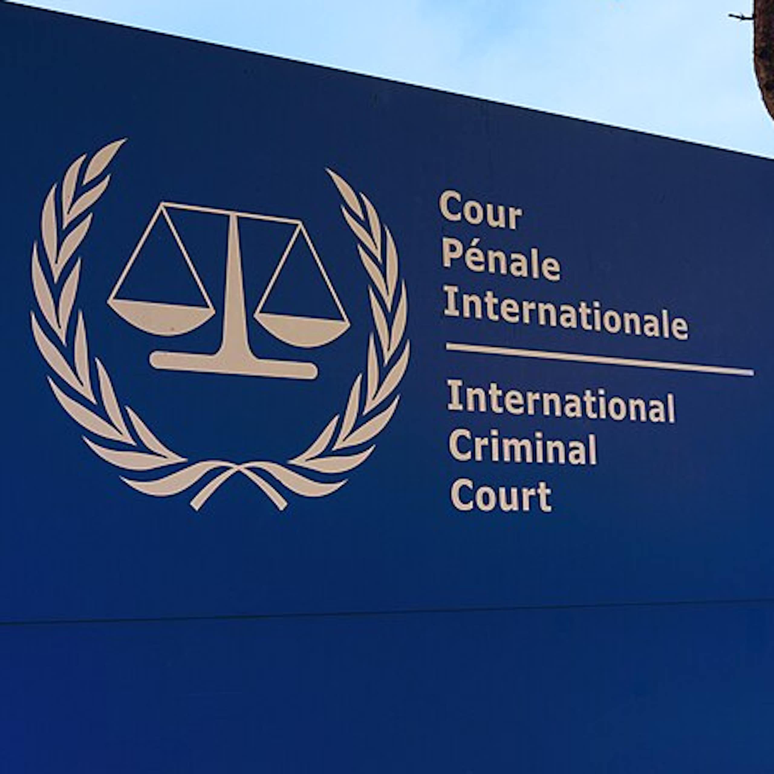 A blue and white sign reads International Criminal Court in English and French in front of a building.