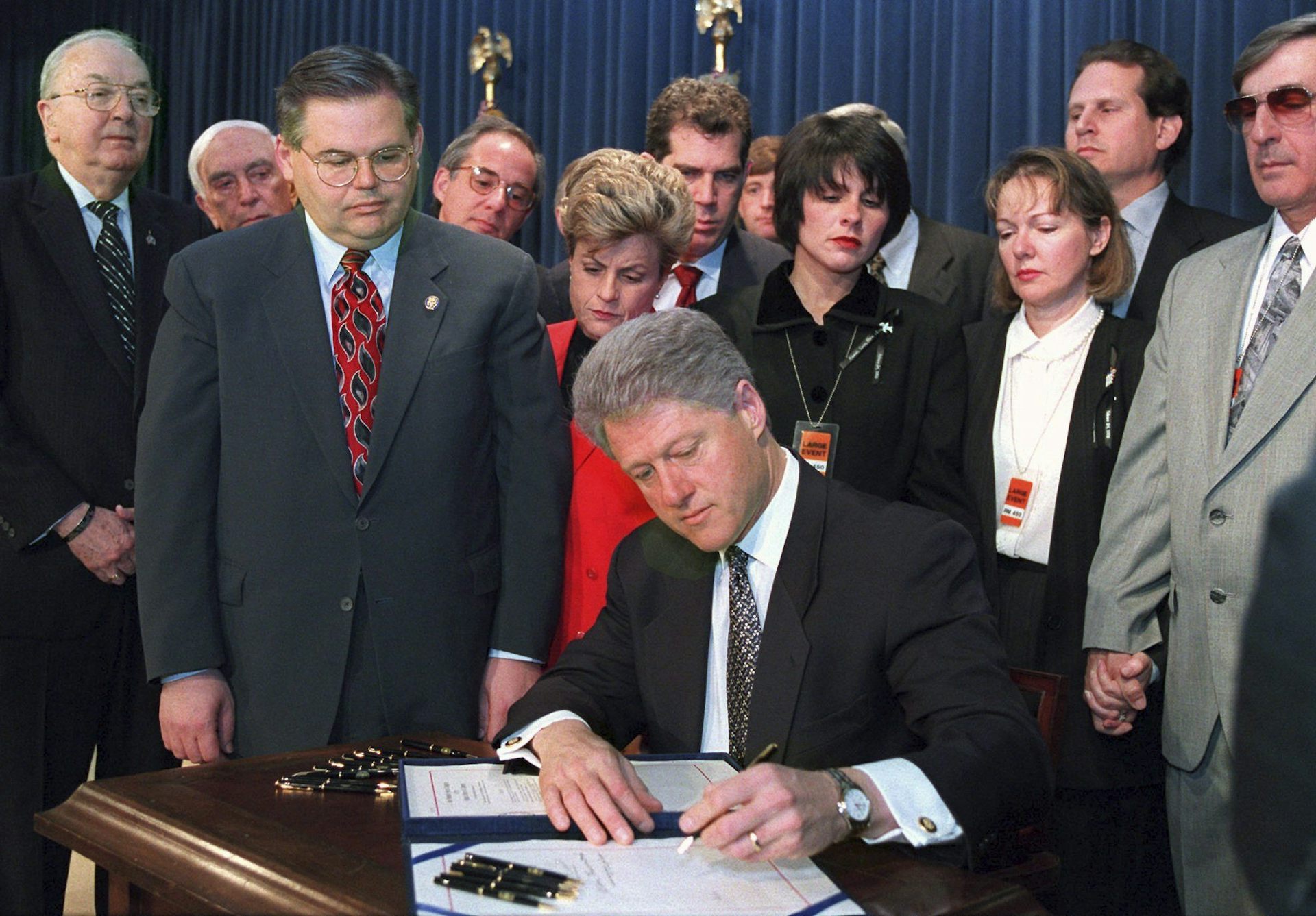 A man with thick dark grey hair signs a bill at a desk.