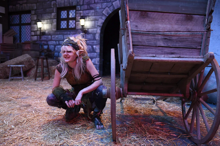 A woman in costume as a gnome warlock crouches next to a stage prop.