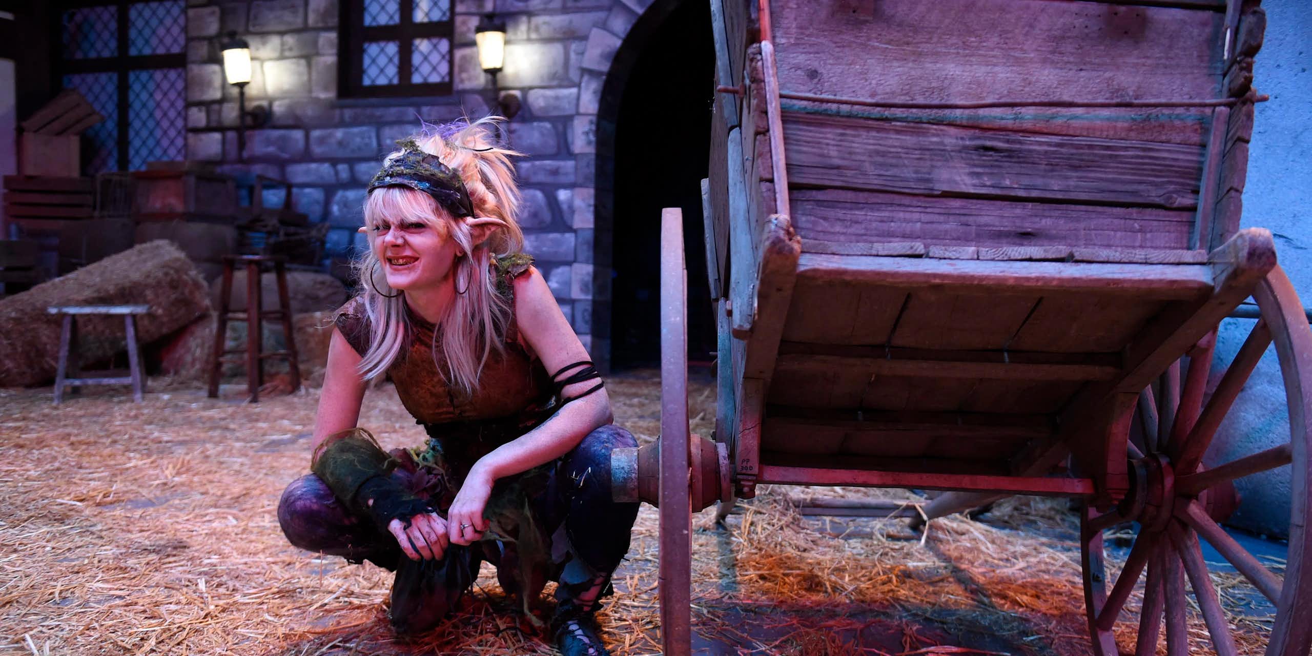 A woman in costume as a gnome warlock crouches next to a stage prop.