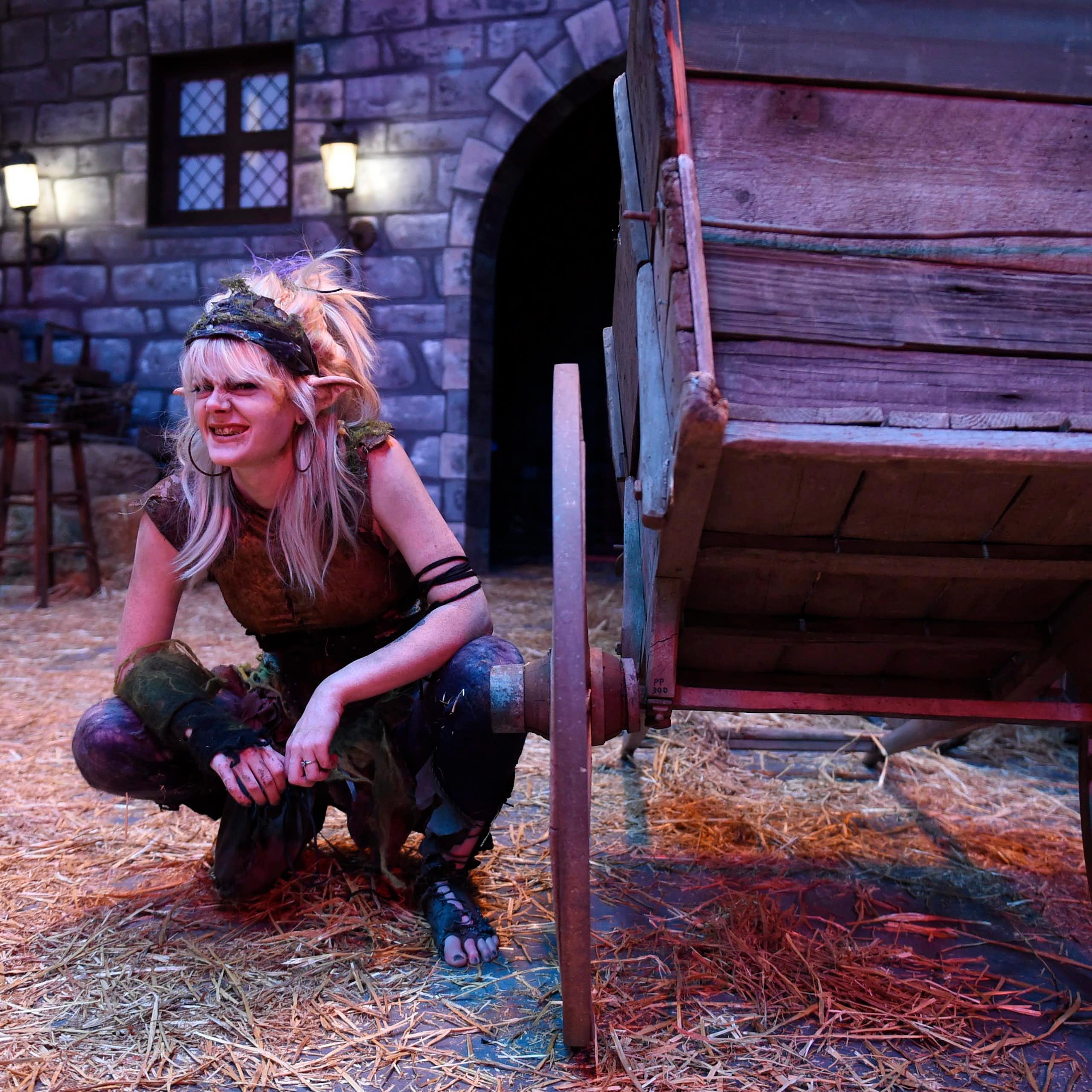 A woman in costume as a gnome warlock crouches next to a stage prop.