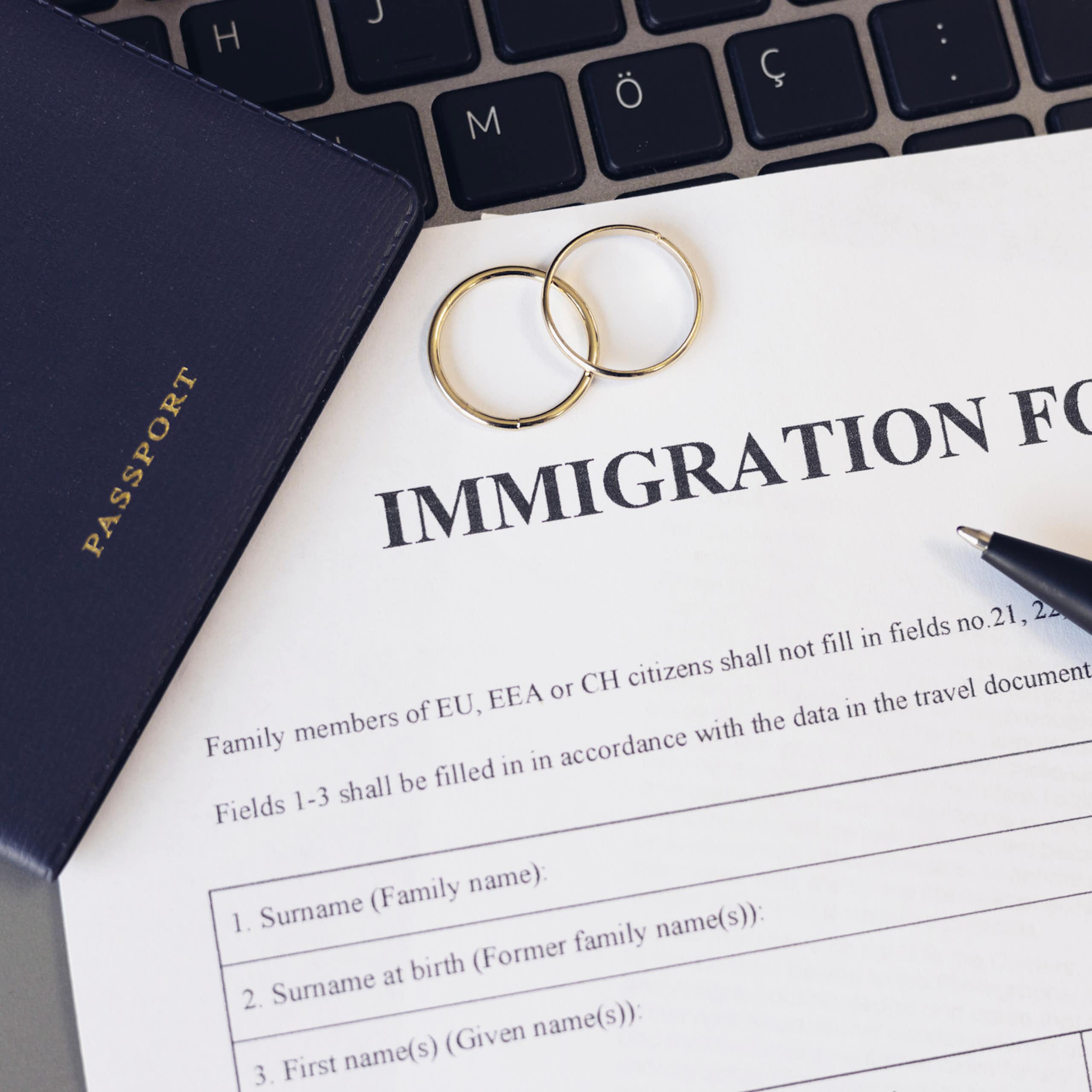 A white form that says 'immigration form' at the top rests near a passport, a pen and two gold rings.
