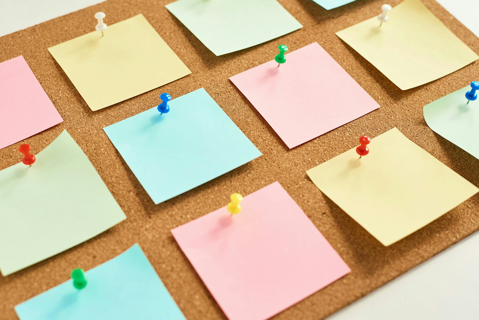 A corkboard with different coloured squares of paper attached to it with push pins.