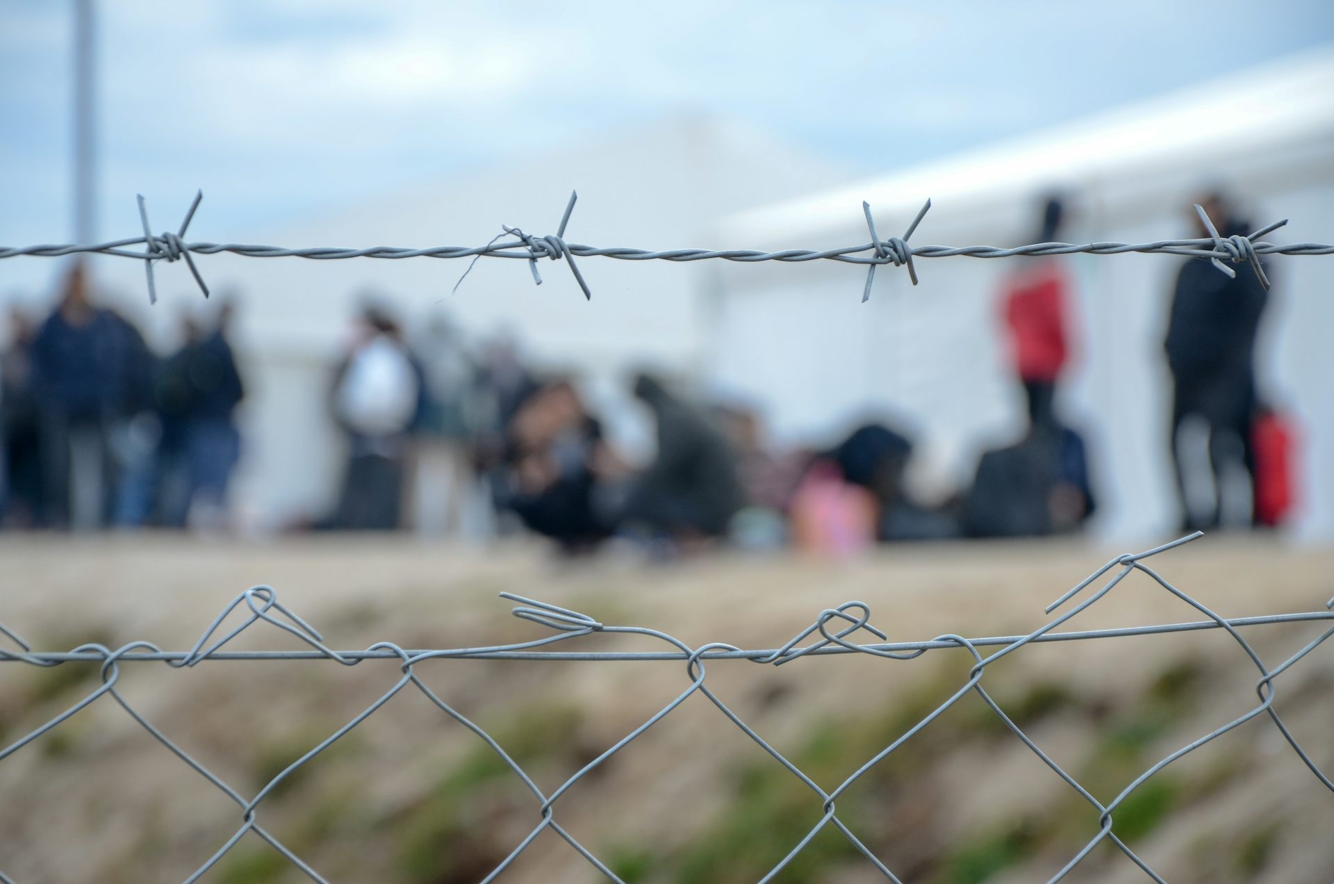 Barbed wire at a refugee camp, with people out of focus in the background