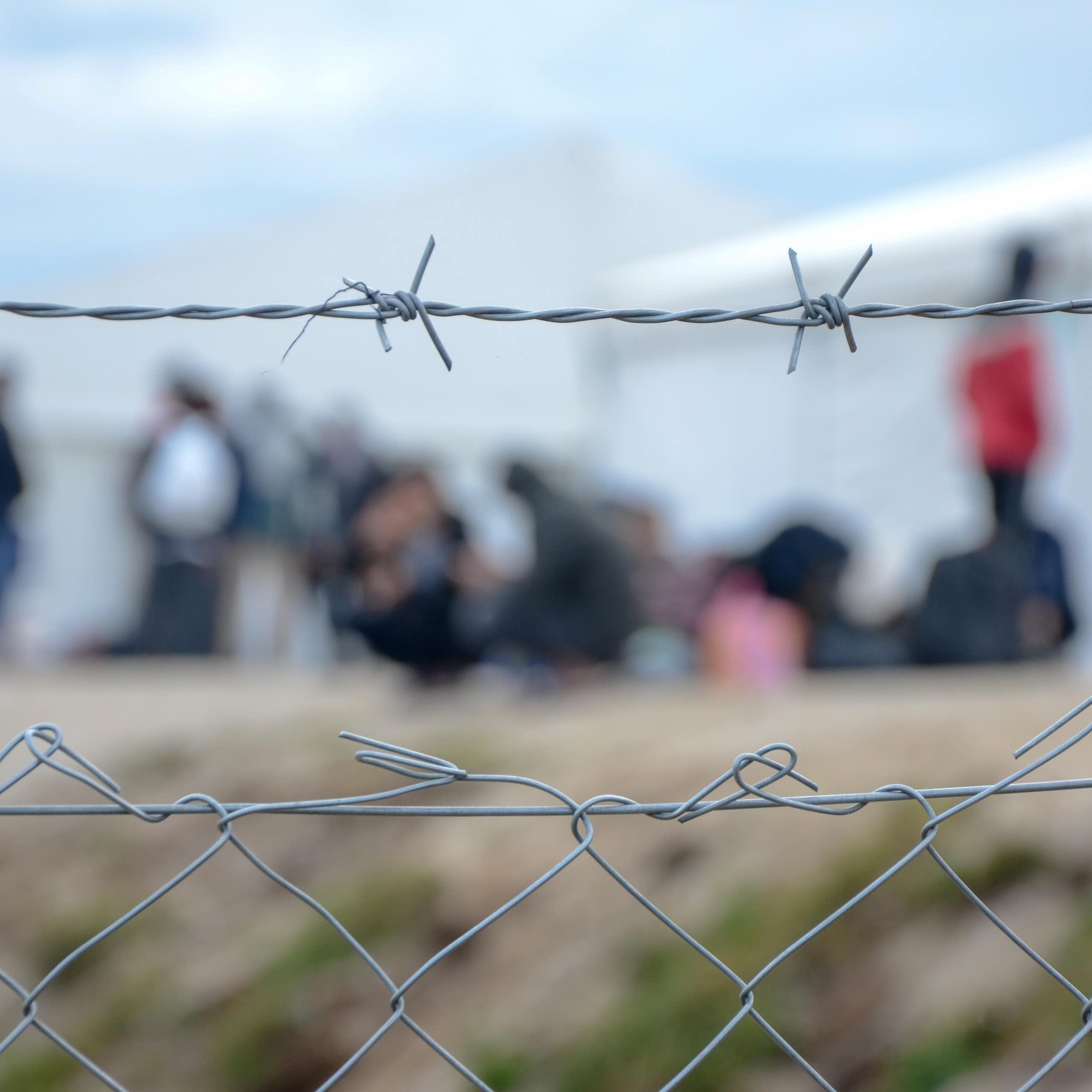 Barbed wire at a refugee camp, with people out of focus in the background