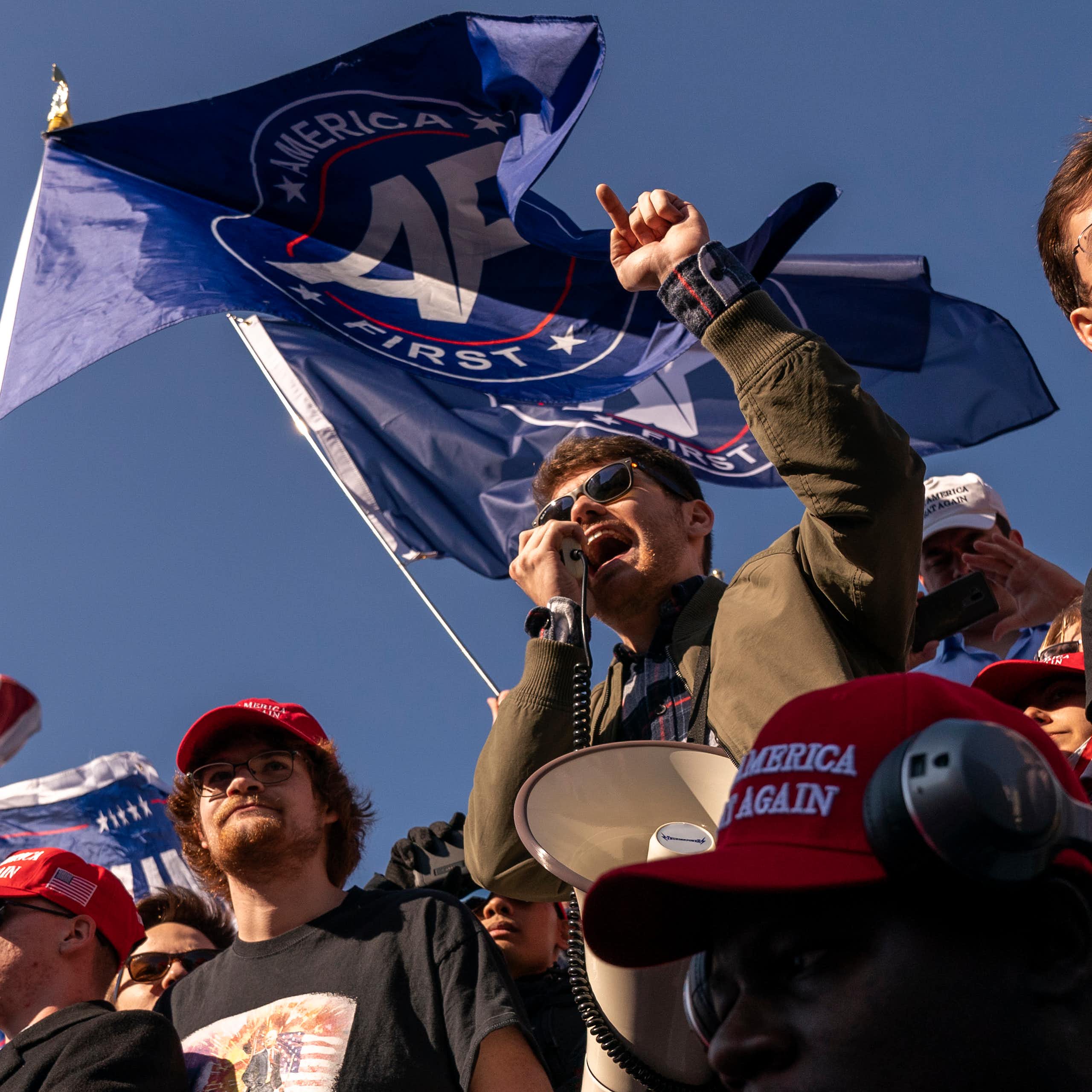 Young man at a rally speaking into a microphone, surrounded by other young men.