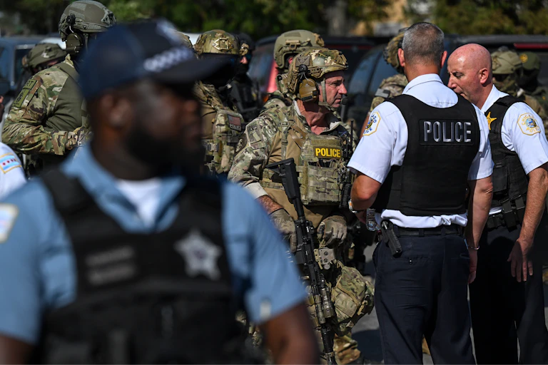 Federal agents in tactical gear and camouflage converse with local police officers wearing black vests.