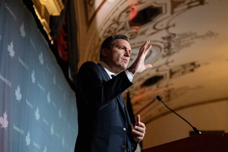 Un hombre de traje habla detrás de un atril.