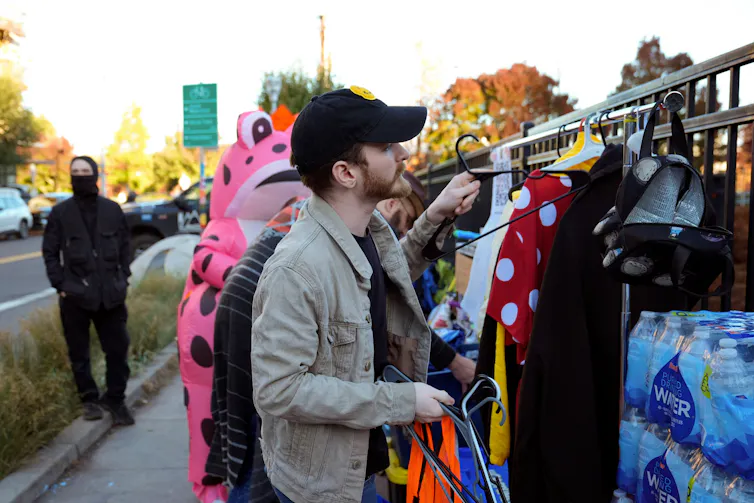 A man wearing a hat sorts things hanging on a rack outside.