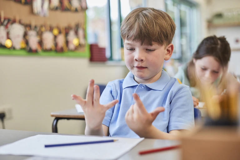 A school boy uses his fingers to count at a classroom desk.