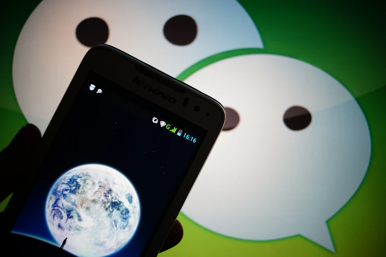A mobile phone in front of an icon with two white speech bubbles resembling faces.