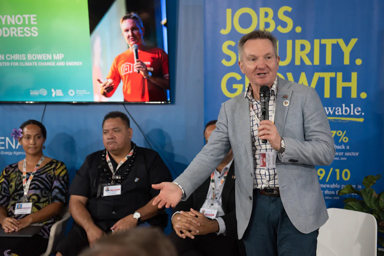 Chris Bowen stands with a microphone in front of a group of people at a conference session in Brazil.