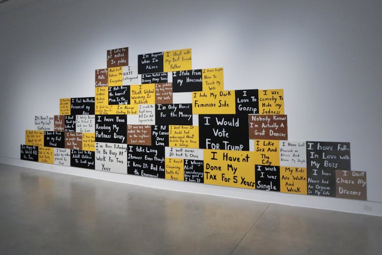 A bunch of peg boards are laid out in an irregular shape across a white wall, with text on each one.