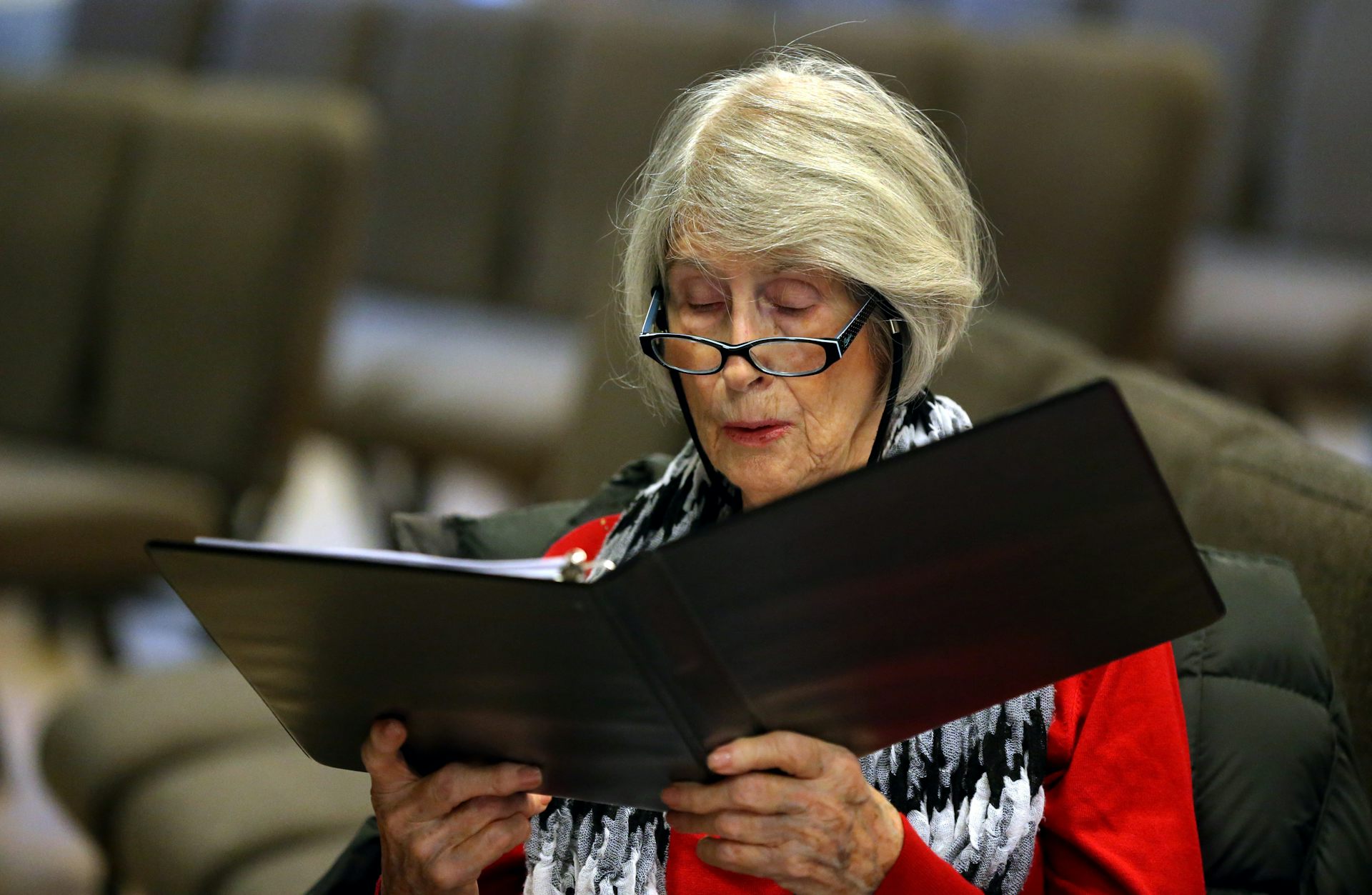 An older woman sings from her music sheet.
