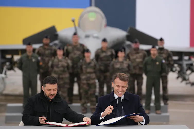 Zelensky and Macron sign a letter at an air base in France.
