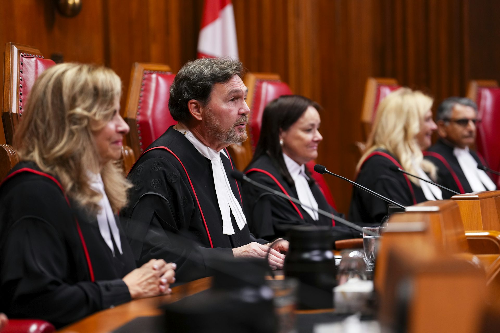 A bearded man in judicial robes sits among three women and another man.