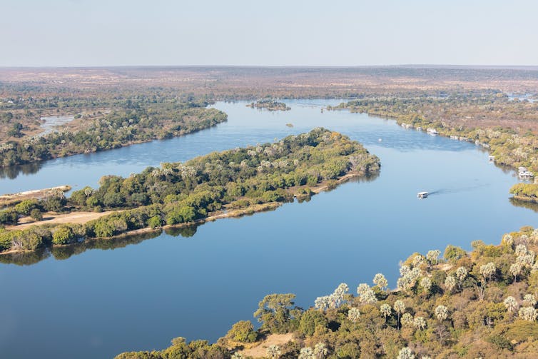 An aerial view of a vast river with a boat on it, wilds all around it.